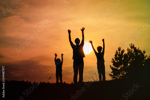 happy father with son and daughter silhouettes play in sunset