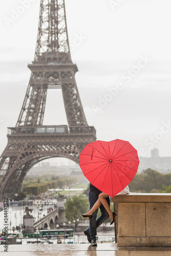 Romantic couple hiding behind heart shaped red umbrella in front of the Eiffel tower