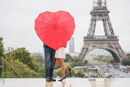 Sticker Romantic couple hiding behind heart shaped red umbrella in front of the Eiffel t
