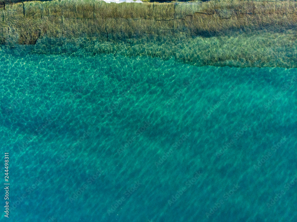 Beach from above taken with a drone showing golden sand and clear blue sea.