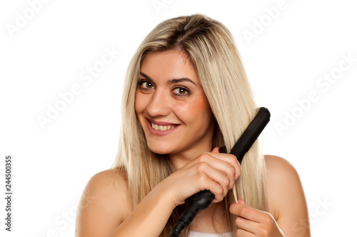 smiling young woman ironing her hair with hair iron on white backgrund