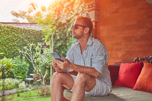 Man using smart phone on a terrace sofa in summertime. photo