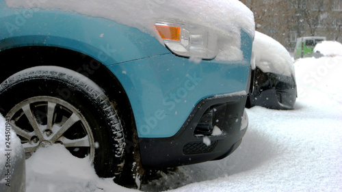 Car wheels stuck in snow drift. Wheel of blue passenger car is stuck in snow. Adverse weather conditions.