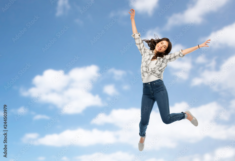 motion, freedom and people concept - happy young woman or teenage girl jumping over blue sky and clouds background