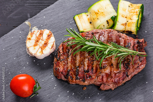 Juicy medium rare beef steak slices on ceramic board with herbs spices and salt.