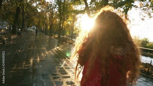 Young caucasian womanwalking in a colorful autumn park by wet alley, enjoying autumn foliage, turns around joyfully smiling at camera. In movement, slow motion. Rare view photo