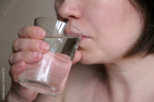Woman drinking clean water from a glass close-up, selective focus. Concept of thirst, healthy lifestyle, water purification, skin care