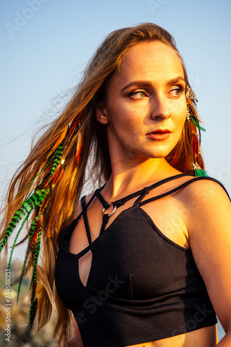 portrait of stylish elegant redheaded chestnut blonde young girl in indie bohemian bo-ho style clothes black stylish top.boho woman long hair,makeup and green feathers in head on the rocks by the sea © yurakrasil