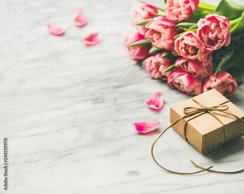 Valentines day holiday background. Bouquet of pink tulips and gift box with ribbon over white marble table background. Pink tulips and gift box with copy space. Lovers or Womens day greeting card photo