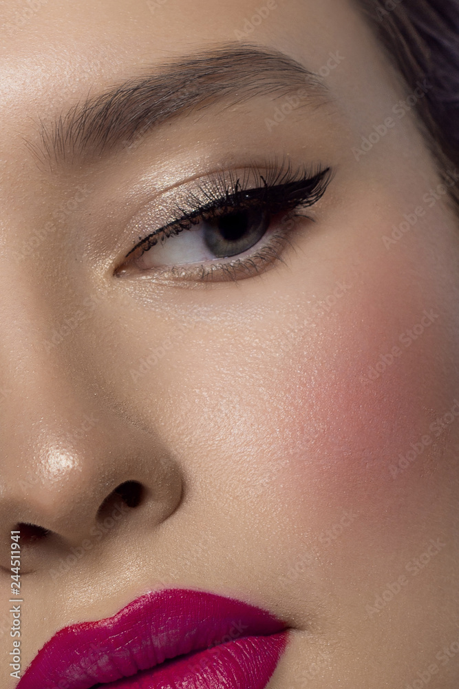 Fototapeta premium Close-up beauty of a half female face with creative fashion evening make-up. Black arrows on the eyes and extremely long eyelashes, on plump lips matte pink lip color. Well-groomed skin after spa