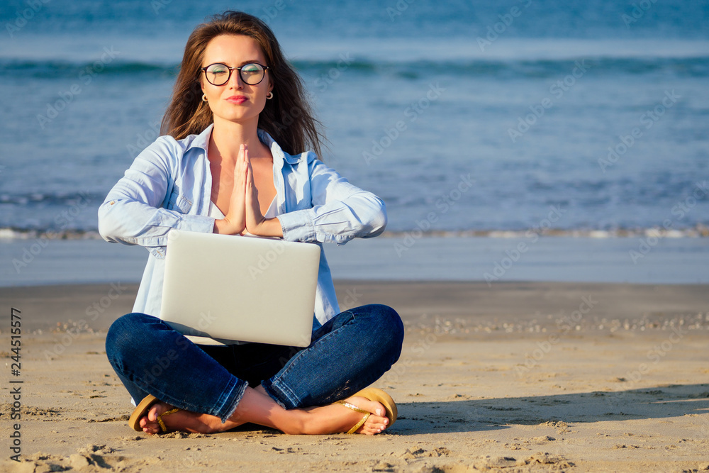 Young calm woman in glasses with laptop freelancing on the tropical paradise beach. Girl freelancer sitting in a summer sand on the seashore dream remote work indian ocean background copyspace