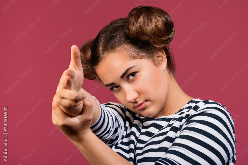 Cool and carefree teen girl tilting head making faces and pointing with finger gun gestures at camera isolated over pink background Cool and carefree teen girl tilting head making faces and pointing with finger gun gestures at camera isolated over pink background