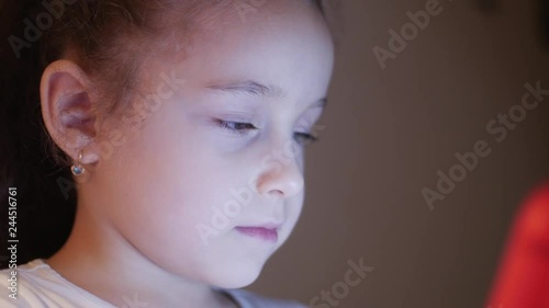 Night Shot of a Cute Caucasian Little Girl Close Up of a Child's Face Viewing a Tablet PC With a Reflection of Pight and Pictures in His Eyes photo