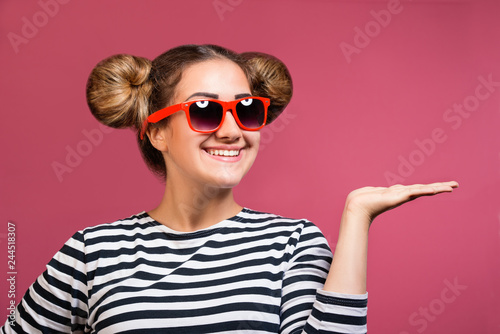 Hipster girl in sunglasses with funny hairstyle showing product with open hand palm with copyspace, isolated
