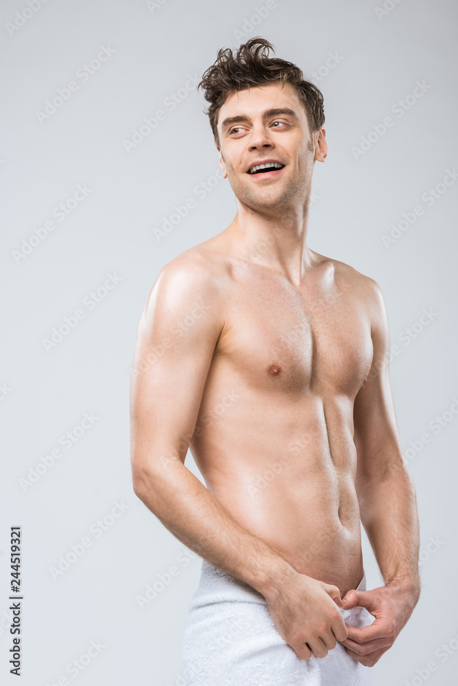 handsome cheerful shirtless man posing in towel isolated on grey