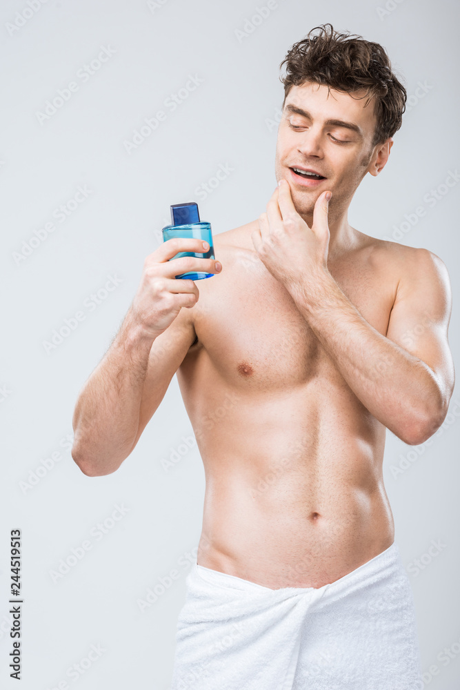 handsome man looking at bottle with cologne, isolated on grey handsome man looking at bottle with cologne, isolated on grey