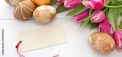 Fototapeta Naklejka Na Ścianę i Meble -  Easter card with bouquet of pink tulips and colorful eggs on white wooden .
