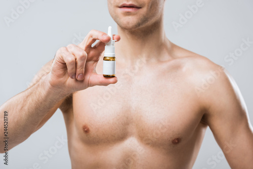 cropped view of shirtless man holding nose spray, isolated on grey