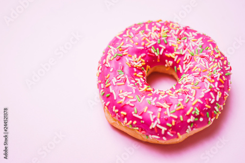 Bright donut in a pink glaze with a multi-colored rainbow sprinkle on a pink background. 