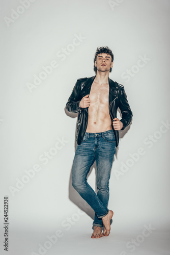 handsome sexy man posing in jeans and black leather jacket on grey