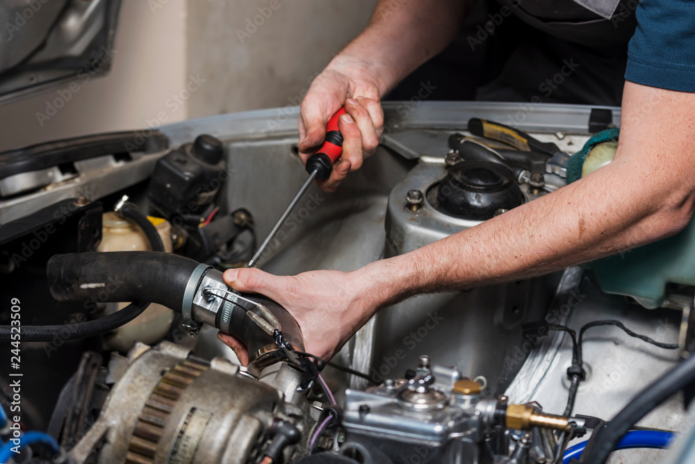 Man's hands with a screwdriver repairing the old car inside of the garage.