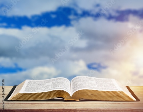 Open book on old wooden table on sky background sunlit
