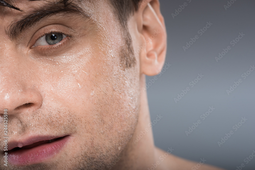 Obraz premium handsome young man with water drops on face, isolated on grey