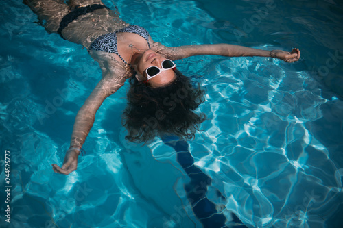 A young girl in sunglasses swims in the pool. Beautiful woman resting in the water in the outdoor pool