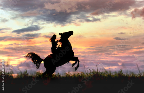 Fototapeta Naklejka Na Ścianę i Meble -  Сowgirl riding rearing stallion standing hind legs on horizon line. Atmospheric sunset with female and horse silhouette before storm on сolorful, cloudy stormy sky background. 
