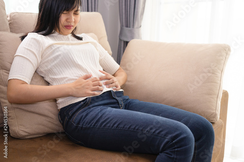 Woman touching or pain on her belly at living room - stomachache concept