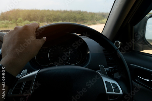 Traveling hand of man use wheel inside of family car. Driving on the nature of country soil road with forest on beside.