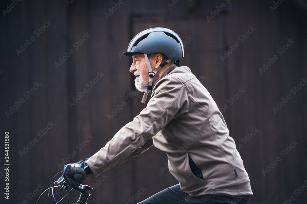 Active senior man with bike helmet cycling outdoors againts dark background. Active senior man with bike helmet cycling outdoors againts dark background.