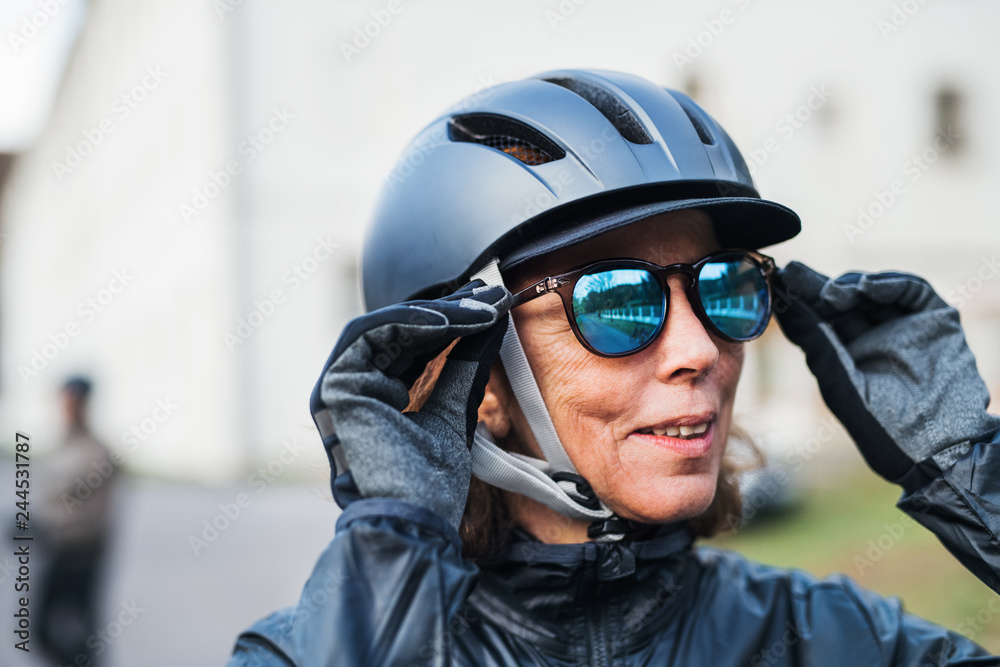 An active senior woman with bike helmet standing outdoors, putting on sunglasses. An active senior woman with bike helmet standing outdoors, putting on sunglasses.