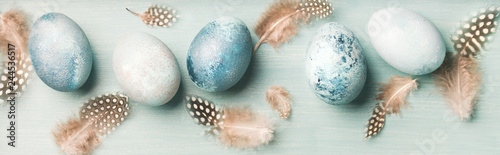 Painted traditional eggs for Easter holiday and feathers over light blue background, top view, wide composition photo