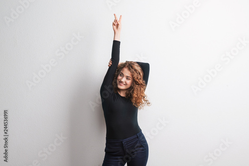 A young beautiful cheerful woman standing in studio, fingers forming V for victory.