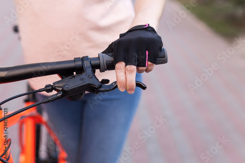 A girl in bicycle gloves holds her hand on the handlebars, clamping the brakes.