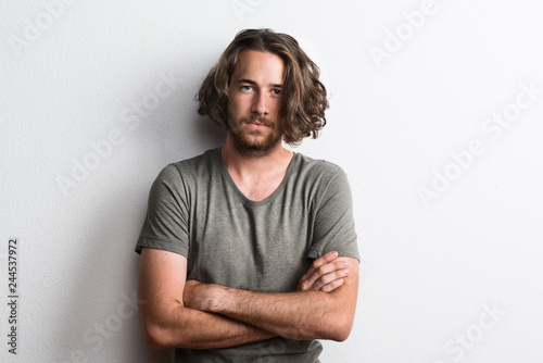 Portrait of a joyful young man with long wavy hair in a studio arms crossed. photo