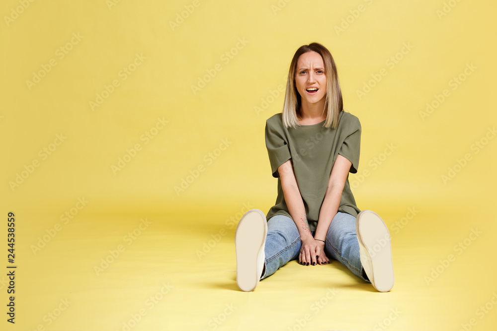 Funny positive whimsical young woman posing sitting on the floor on a yellow background. Place for advertising Funny positive whimsical young woman posing sitting on the floor on a yellow background. Place for advertising