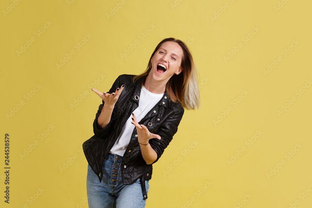 Rock'n'roll. Naughty positive young woman dances in a leather jacket on a yellow background in the studio. Place for text Rock'n'roll. Naughty positive young woman dances in a leather jacket on a yellow background in the studio. Place for text