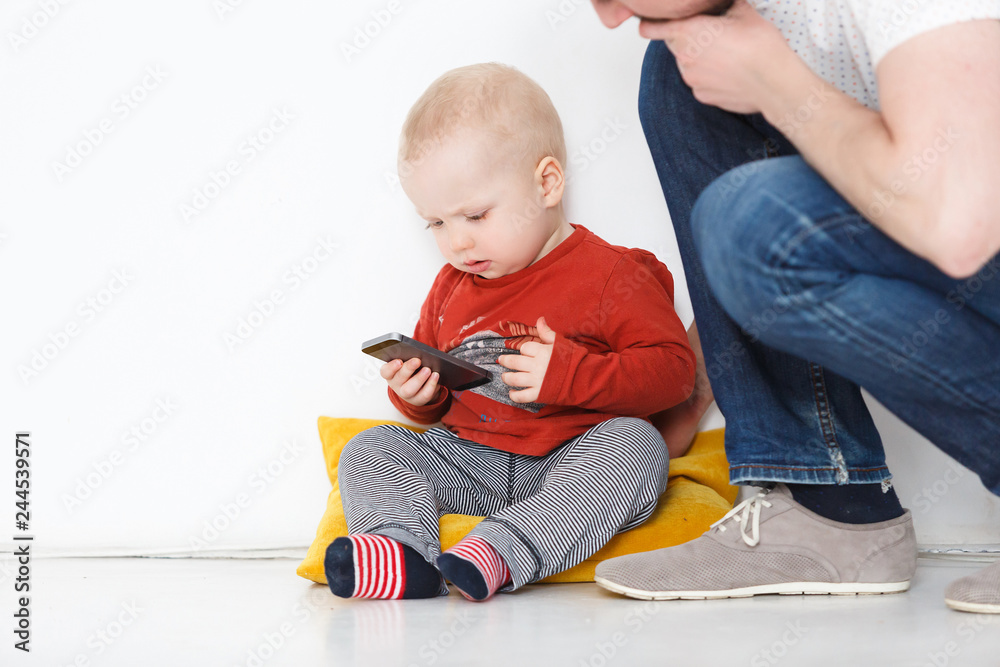 Life with gadgets - small pretty child holding a smartphone and looking at the screen trying to understand the game near with unknown daddy. Copyspace Life with gadgets - small pretty child holding a smartphone and looking at the screen trying to understand the game near with unknown daddy. Copyspace