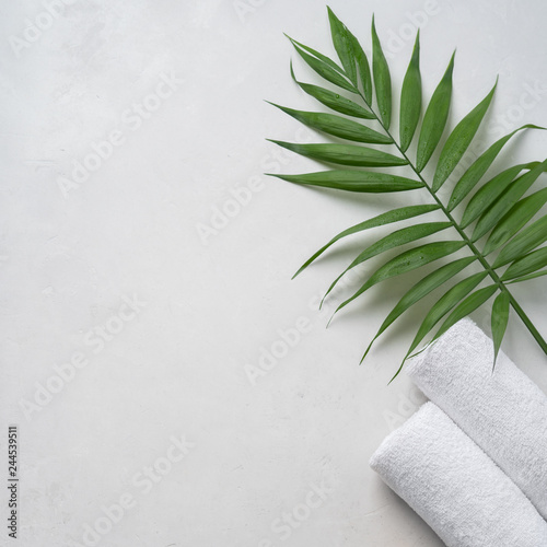 Spa concept: two white fluffy towels twisted into rolls on a light surface with a palm leaf with copy space, flat lay