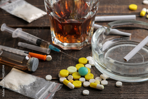 Various addictive drugs including alcohol, cigarettes, and drugs on a brown wooden table. Drug addiction concept photo