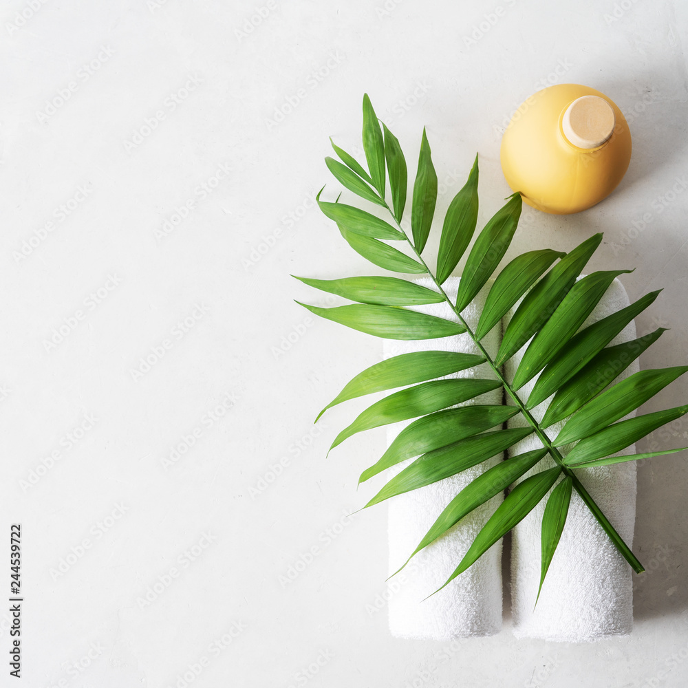 Spa concept: beautiful ceramic bottle, white towels and palm leaf on concrete light surface with copy space, flat lay.