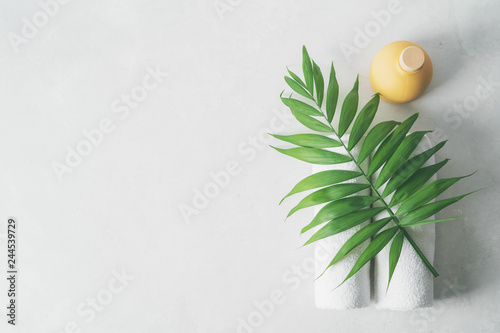 Spa concept: beautiful ceramic bottle, white towels and palm leaf on concrete light surface with copy space, flat lay.