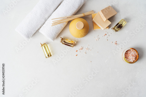 Flat lay spa composition with towels, aroma fragrance bottle, handmade organic soaps, oil frangipani, sandal wood, patchouli, pink salt on light concrete surface with copy space.