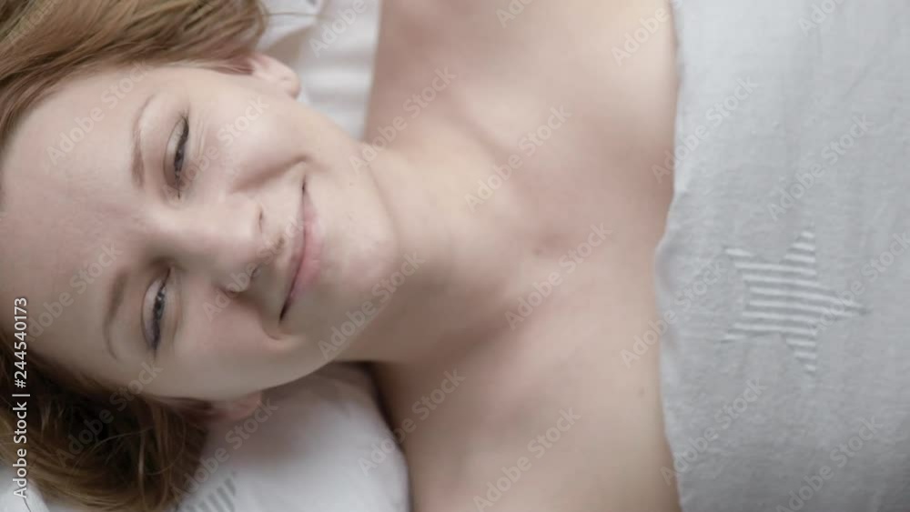 Lovely young Woman Lies in Bed Covered with Blanket. Top view of Girl is Shy and Cover of her Face with Blanket. Female Smiling and Looking at Camera. Lovely young Woman Lies in Bed Covered with Blanket. Top view of Girl is Shy and Cover of her Face with Blanket. Female Smiling and Looking at Camera.