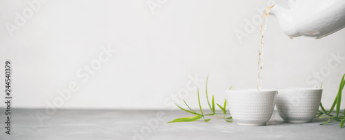 Panel kuchenny z motywem Female hand pouring green tea from a teapot into cups on white background with copy space. Long wide banne with Asian tea set.