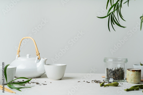 Asian tea concept, two white cups of tea and teapot surrounded with green tea dry leaves , space for a text on white background. Brewing and Drinking tea.