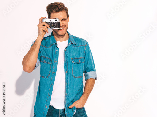 Portrait of handsome smiling man wearing summer hipster jeans clothes. Model male holding vintage photo camera. Isolated on white