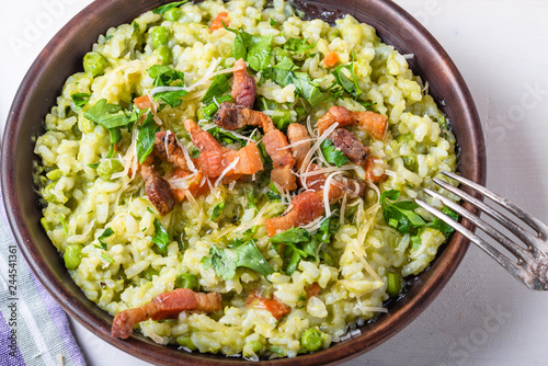 Traditional Italian risotto with peas, carrots and fried bacon, pancetta in rustic style, close-up